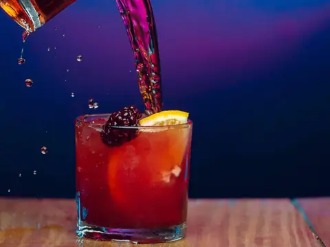 Drink vermelho sendo servido sobre o gelo, com amora e laranja